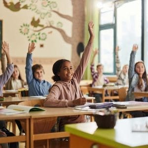Classroom of small children with their hands raised